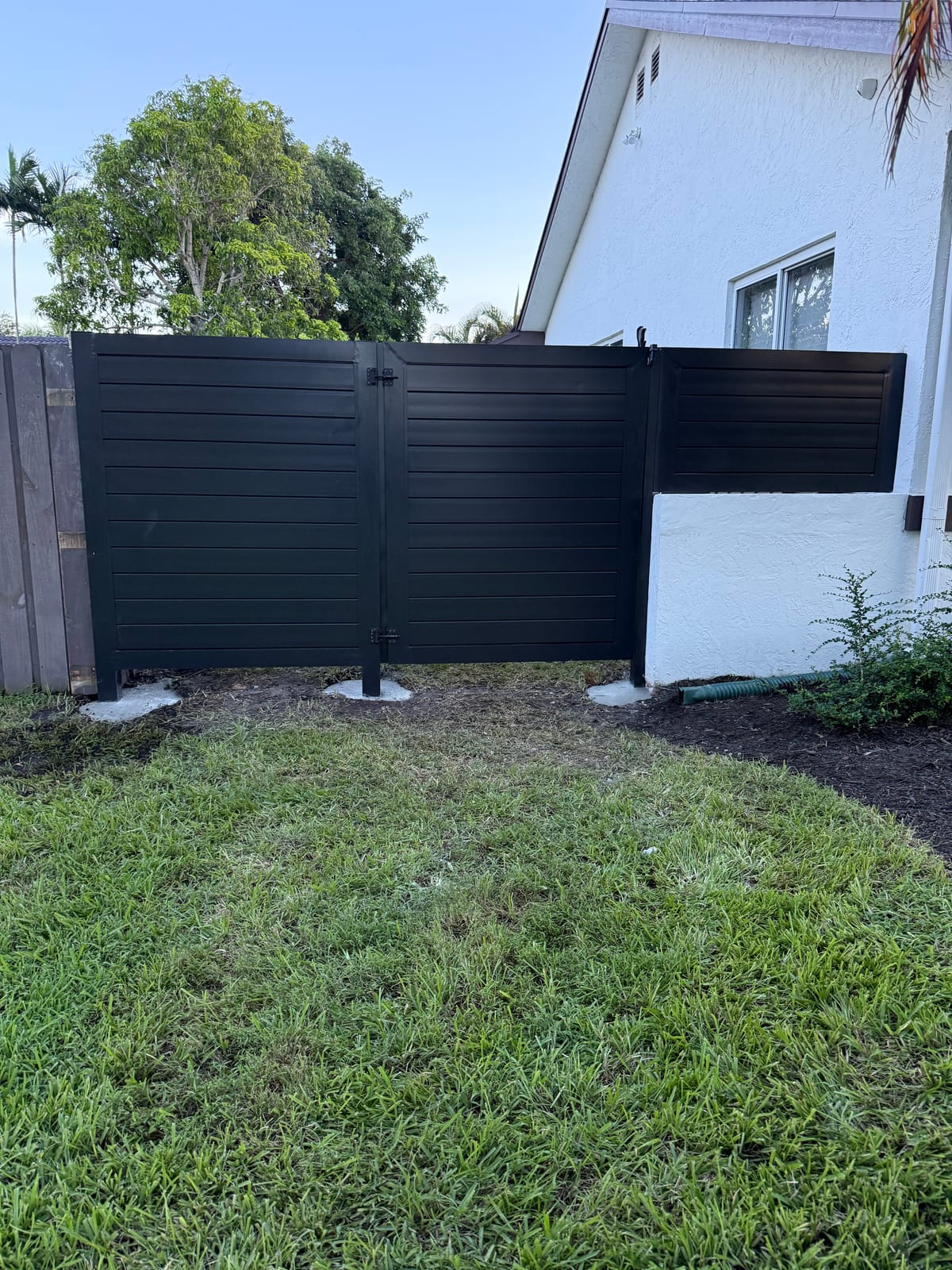 Black aluminum double-swing driveway gate matching a horizontal-slat privacy fence