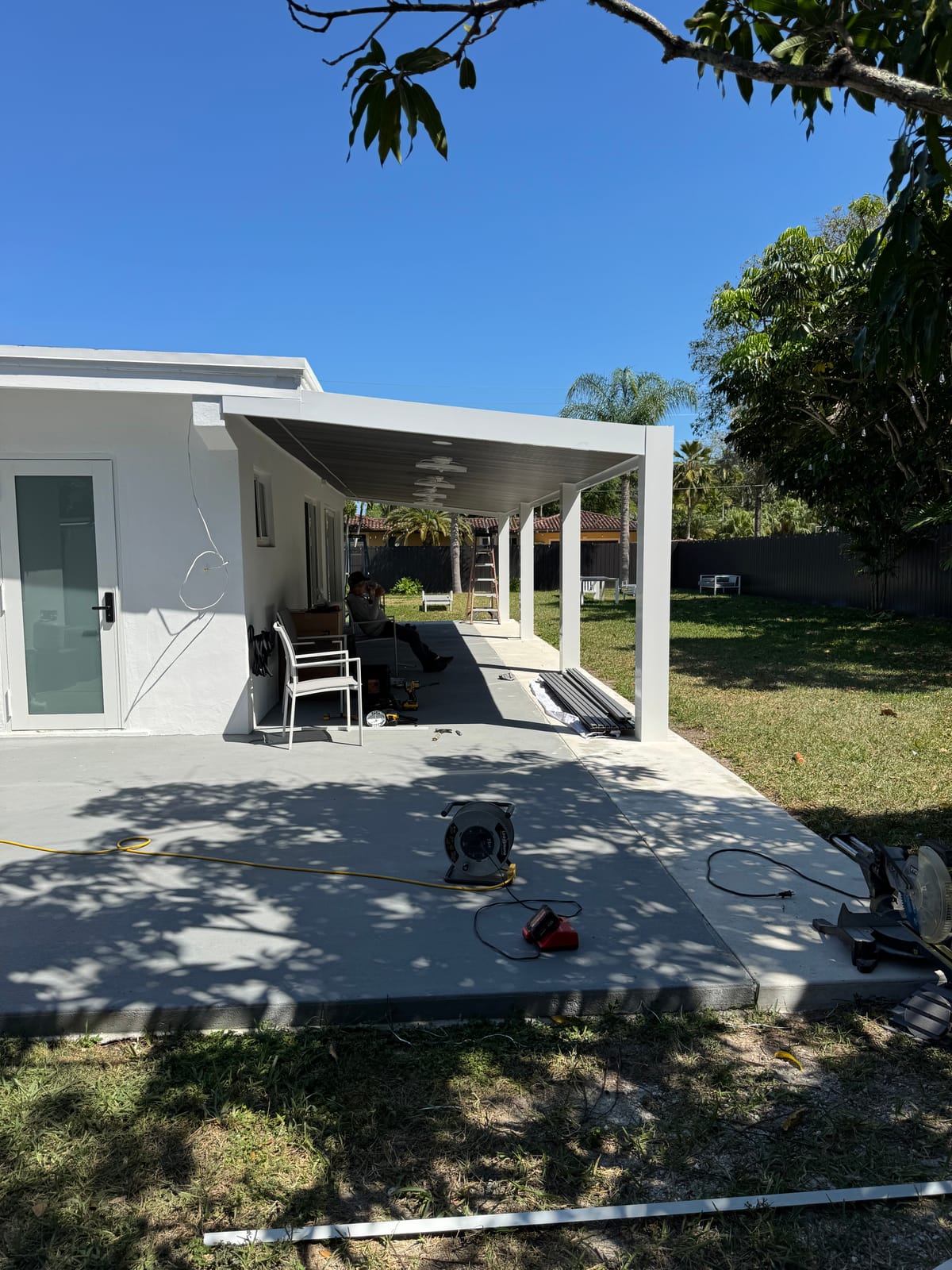 Modern white pergola attached to a home, shading a back patio in South Florida