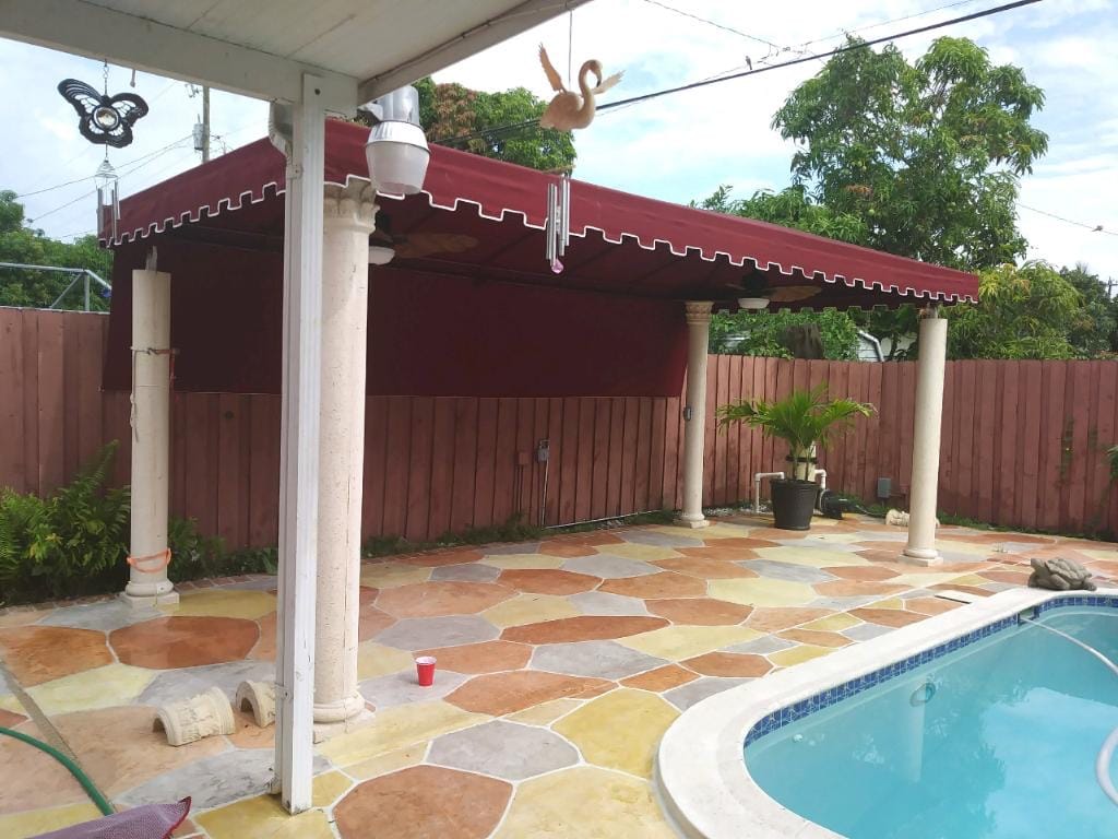 Burgundy patio awning on decorative columns beside a pool with a wood privacy fence